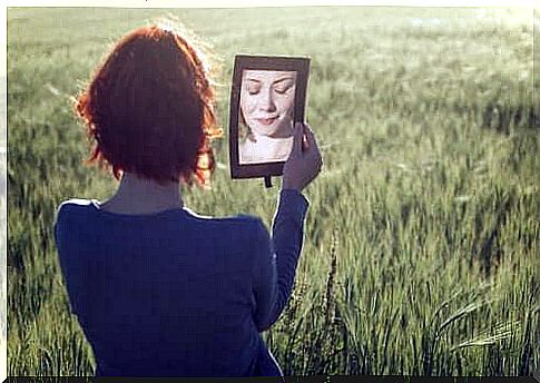 A red-haired woman holds up a mirror in front of her own face while closing her eyes.