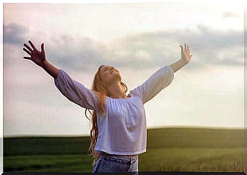 Happy woman in field stretching her arms up in the air