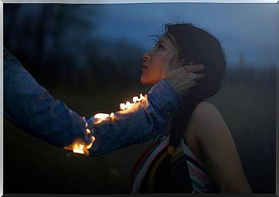 A man with a burning arm reaches out for a woman's face