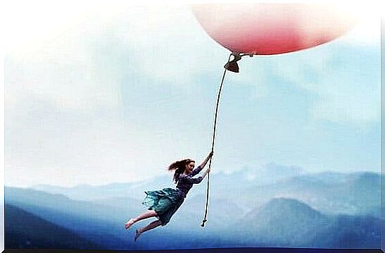 a girl holding on to a giant balloon over the mountains