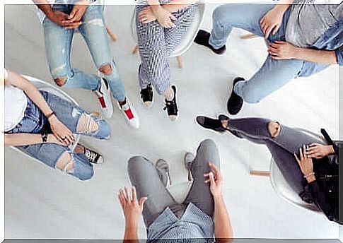 A group of young people sit together in a ring.  We only see their legs and upper bodies.