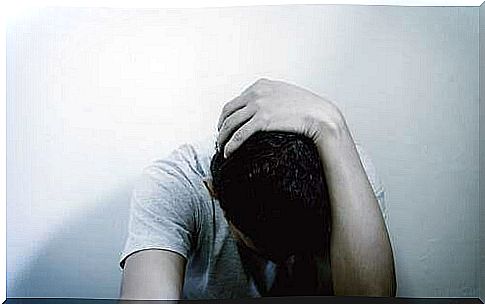 A depressed man hanging on his head while looking at the ground.